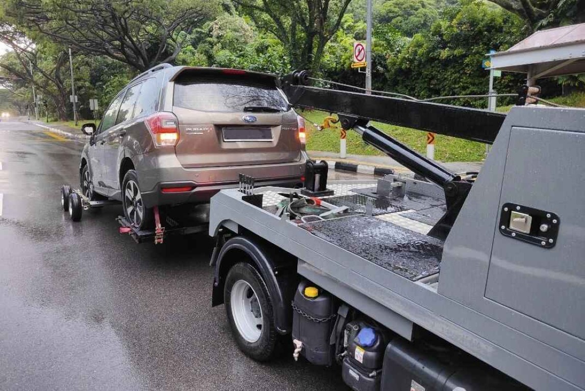 Flatbed tow truck safely transporting a brown Subaru SUV on a wet road in Islip, NY